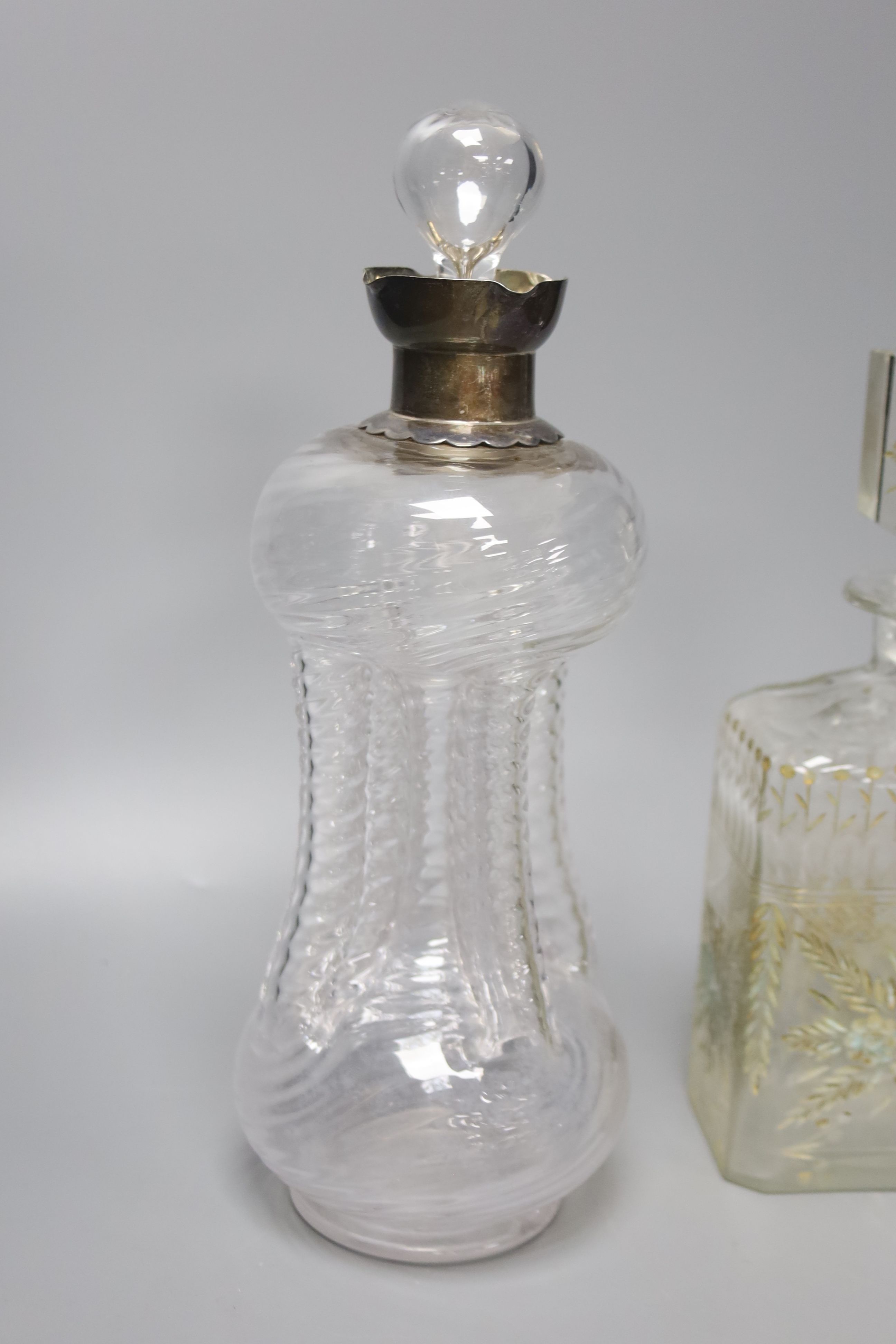 A Victorian wrythen moulded hour glass shaped decanter, with silver collar, 31cm high, togoether with a further 19th century engraved glass decanter (a.f.), 25cm high